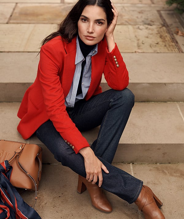 Woman wears orange blazer with striped button-down and dark denim.